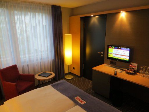 Welcome Hotel, Essen, Deutschland, Zimmer 131 mit Fenster, Sessel, Tisch, Verbindungstür, Flachbildfernseher, Minibar und Schreibtisch
