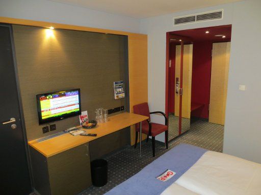 Welcome Hotel, Essen, Deutschland, Zimmer 131 mit Flachbildfernseher, Minibar, Tisch, Stuhl, Schrank mit Spiegel, Kofferablage und Eingangstür